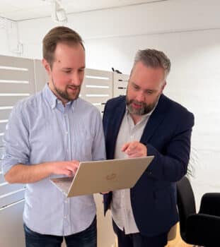 Två kollegor i en kontorsmiljö står och tittar på en laptop